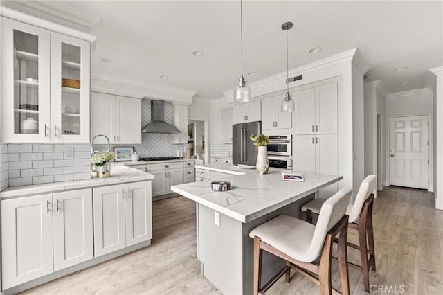 kitchen with gas cooktop, light stone countertops, high end fridge, wall chimney exhaust hood, and a center island