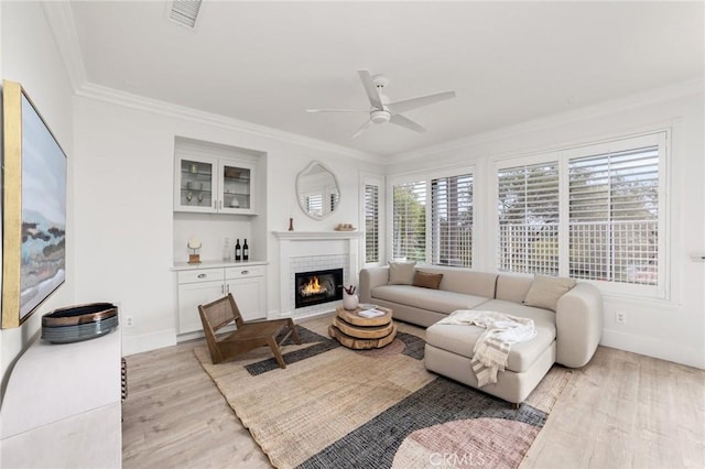 living area featuring a ceiling fan, visible vents, crown molding, a brick fireplace, and light wood-type flooring