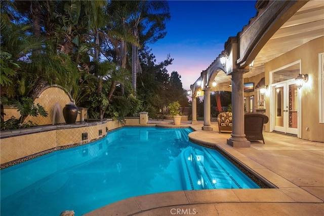 pool at dusk featuring a patio and french doors