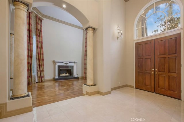 foyer with light wood-type flooring, a towering ceiling, and decorative columns