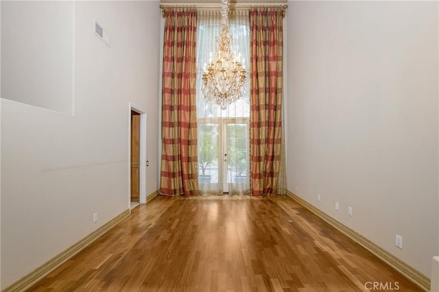 empty room with hardwood / wood-style floors, a chandelier, and french doors