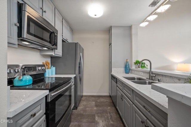 kitchen with sink, gray cabinetry, light stone counters, hanging light fixtures, and appliances with stainless steel finishes