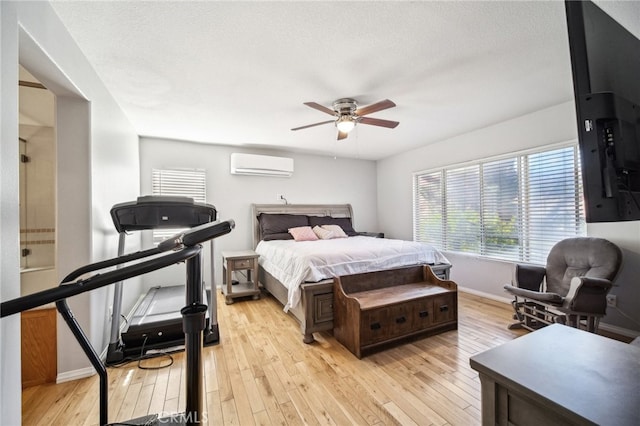 bedroom featuring a wall unit AC, a textured ceiling, light hardwood / wood-style floors, and ceiling fan