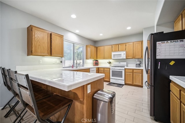 kitchen featuring tile countertops, kitchen peninsula, a breakfast bar, and white appliances