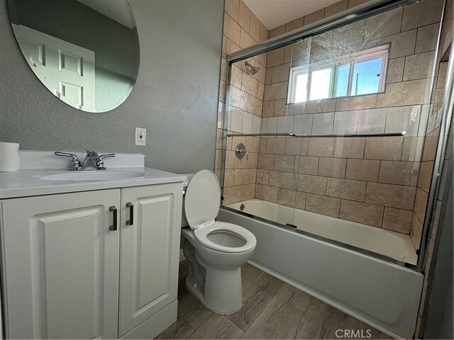 full bathroom with hardwood / wood-style flooring, toilet, vanity, and combined bath / shower with glass door