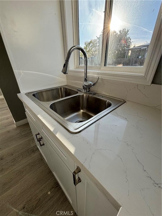 room details with hardwood / wood-style flooring, white cabinetry, sink, and light stone counters