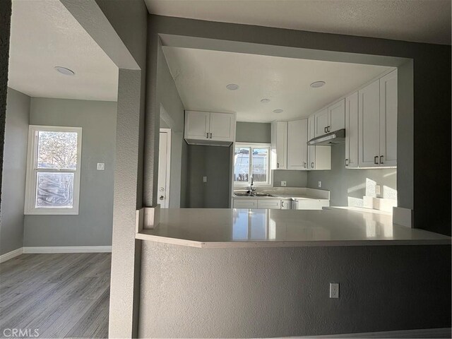 kitchen with white cabinets, plenty of natural light, kitchen peninsula, and light hardwood / wood-style flooring