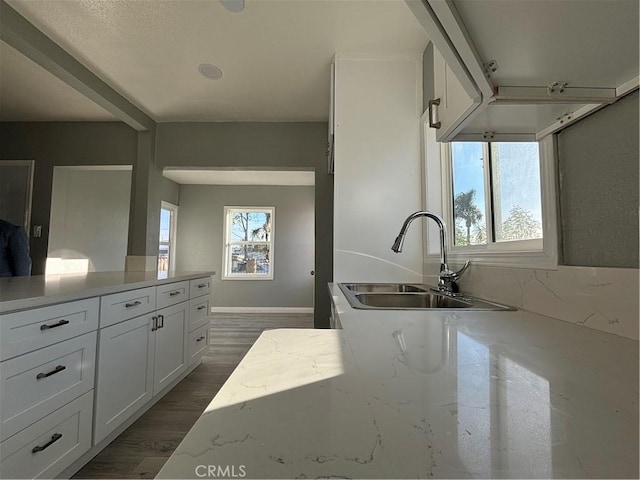 kitchen with dark hardwood / wood-style floors, light stone countertops, sink, and white cabinets