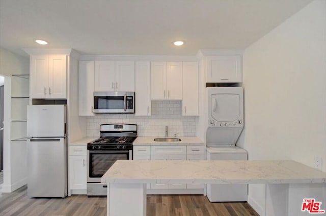 kitchen with sink, white cabinetry, stainless steel appliances, light hardwood / wood-style flooring, and stacked washer and clothes dryer