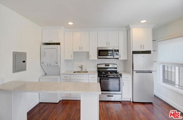 kitchen with stacked washer / drying machine, dark wood-type flooring, sink, white cabinets, and appliances with stainless steel finishes