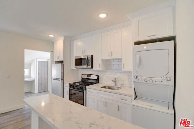 kitchen featuring white cabinets, stainless steel appliances, stacked washer / dryer, and sink