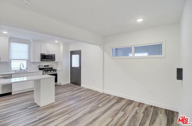 kitchen featuring stainless steel appliances, backsplash, sink, white cabinets, and light hardwood / wood-style floors