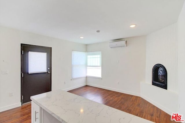 kitchen featuring light stone countertops, an AC wall unit, and dark wood-type flooring