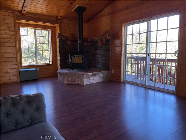 unfurnished living room featuring a healthy amount of sunlight, a wood stove, vaulted ceiling, and dark hardwood / wood-style flooring