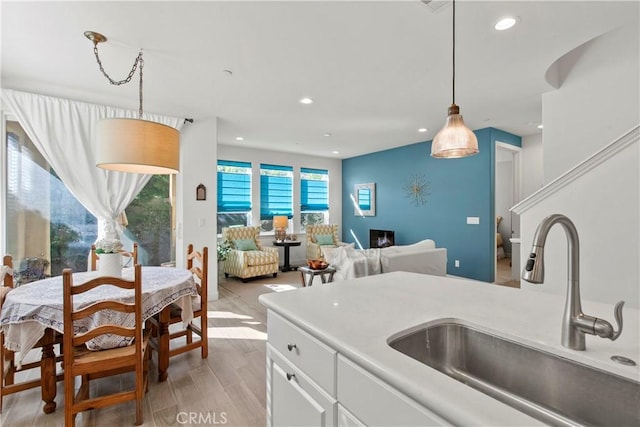 kitchen with white cabinetry, sink, light hardwood / wood-style floors, and decorative light fixtures