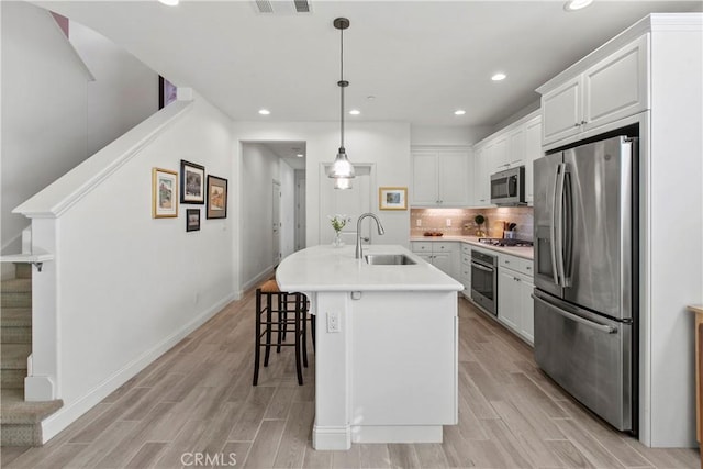 kitchen featuring pendant lighting, sink, white cabinetry, stainless steel appliances, and an island with sink