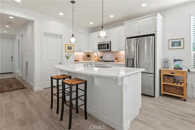 kitchen featuring appliances with stainless steel finishes, an island with sink, sink, white cabinets, and hanging light fixtures