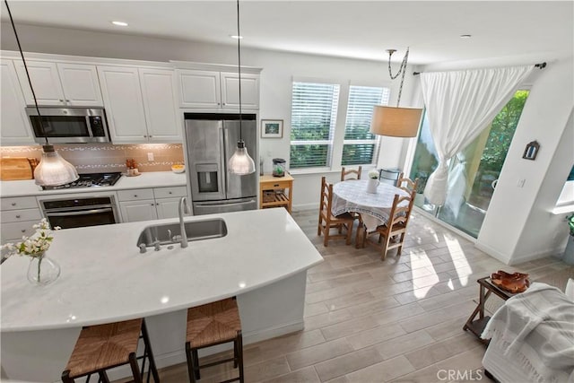 kitchen featuring white cabinetry, hanging light fixtures, a center island with sink, and appliances with stainless steel finishes