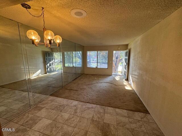 spare room featuring a notable chandelier, a textured ceiling, carpet floors, and lofted ceiling