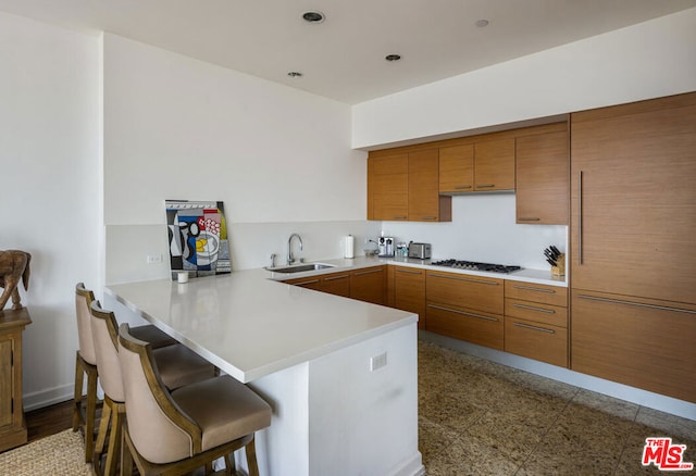 kitchen featuring a kitchen breakfast bar, kitchen peninsula, sink, and gas cooktop