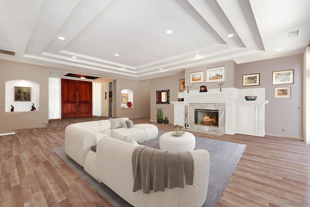 living room with a fireplace, light hardwood / wood-style flooring, and a raised ceiling