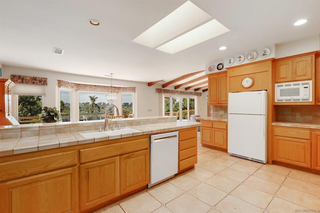 kitchen with a skylight, tile counters, sink, tasteful backsplash, and white appliances