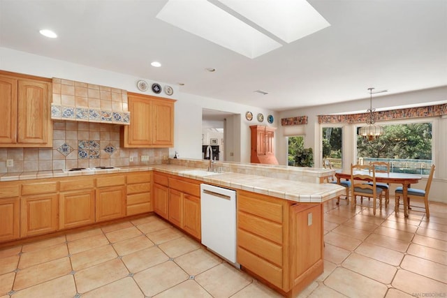 kitchen featuring a skylight, sink, kitchen peninsula, white appliances, and decorative backsplash