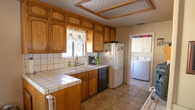 kitchen featuring tasteful backsplash, tile countertops, washer and dryer, dishwasher, and sink