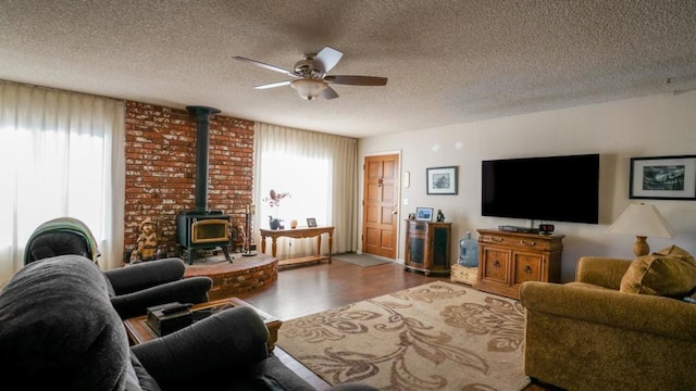 living room featuring a wood stove, a textured ceiling, wood-type flooring, and ceiling fan