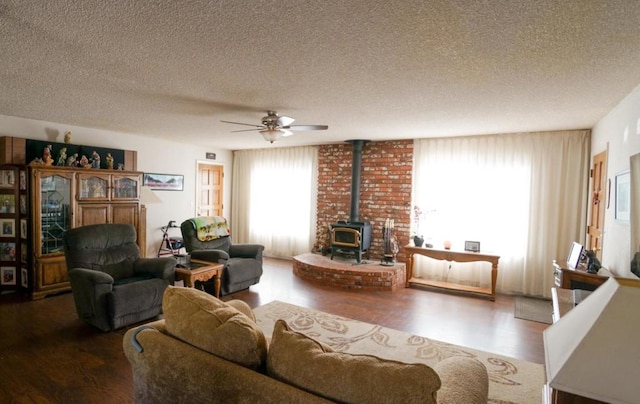 living room featuring ceiling fan, hardwood / wood-style flooring, a textured ceiling, and a wood stove