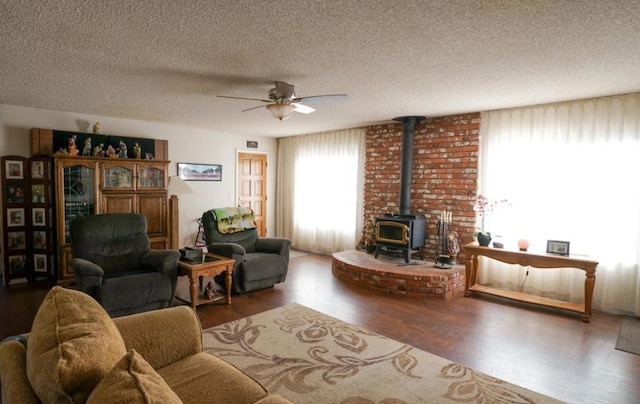 living room featuring ceiling fan, a wood stove, a textured ceiling, and hardwood / wood-style floors