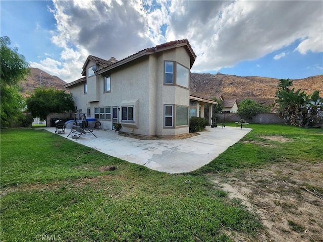 back of house with a lawn, a patio area, a mountain view, and stucco siding