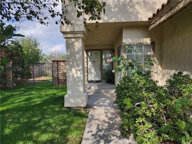 view of exterior entry with a yard, fence, and stucco siding