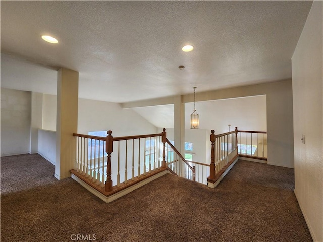 hallway featuring recessed lighting, dark carpet, a textured ceiling, and an upstairs landing