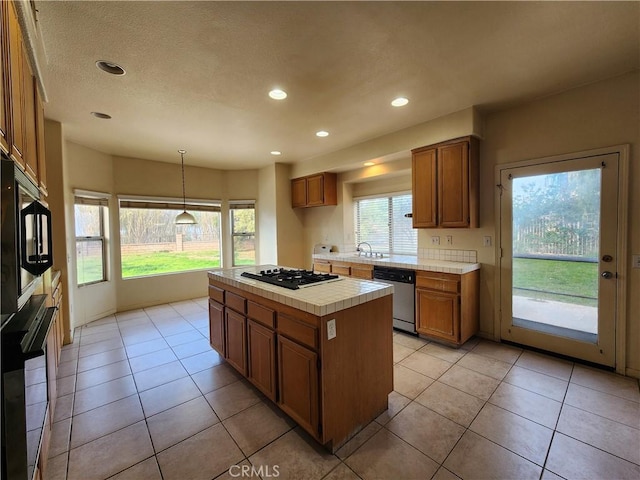 kitchen featuring a center island, tile counters, hanging light fixtures, brown cabinetry, and black appliances