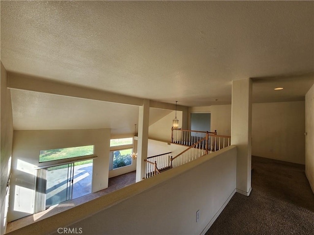 hallway with a textured ceiling, carpet floors, and an upstairs landing