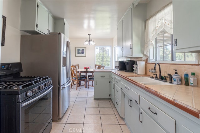 kitchen featuring sink, tile countertops, white cabinetry, pendant lighting, and range with gas stovetop