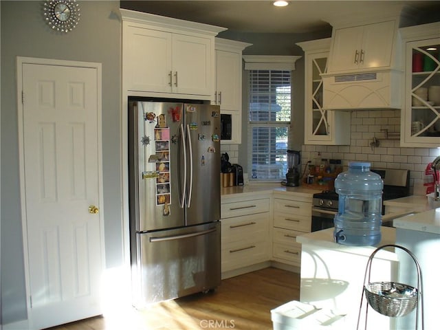 kitchen with custom exhaust hood, white cabinetry, stainless steel appliances, backsplash, and light hardwood / wood-style flooring