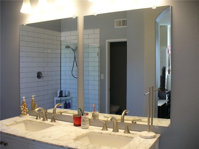 bathroom featuring toilet, vanity, and tiled shower