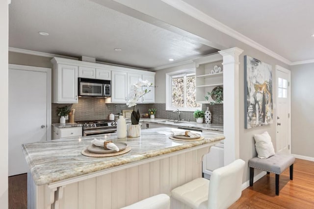 kitchen with light stone countertops, white cabinetry, a kitchen breakfast bar, tasteful backsplash, and appliances with stainless steel finishes