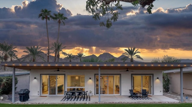 back house at dusk featuring ceiling fan and a patio