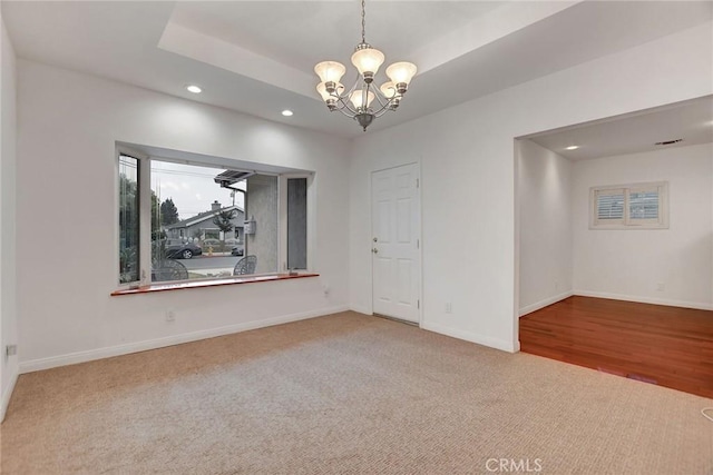 carpeted empty room with a raised ceiling and an inviting chandelier