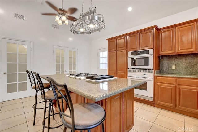 kitchen with light stone countertops, a center island, french doors, white double oven, and a breakfast bar