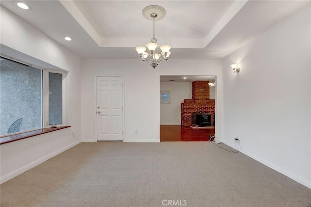 unfurnished living room with carpet floors, a tray ceiling, a brick fireplace, and a notable chandelier