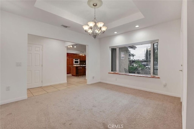 spare room featuring light colored carpet, a tray ceiling, and a chandelier