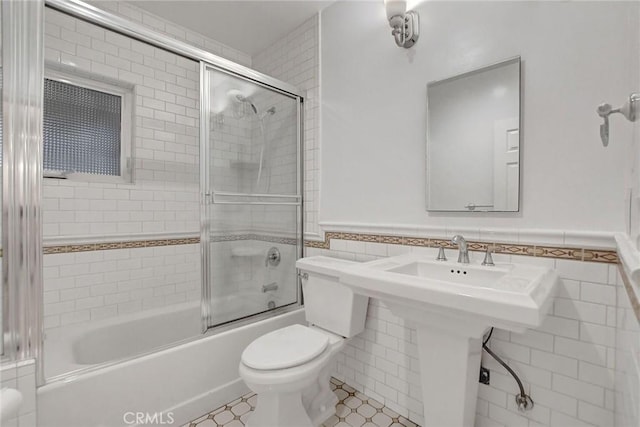 bathroom featuring toilet, combined bath / shower with glass door, tile walls, and tile patterned floors