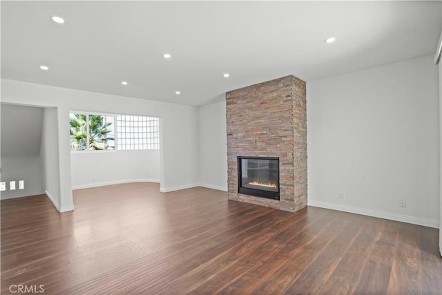 unfurnished living room with a stone fireplace and dark wood-type flooring