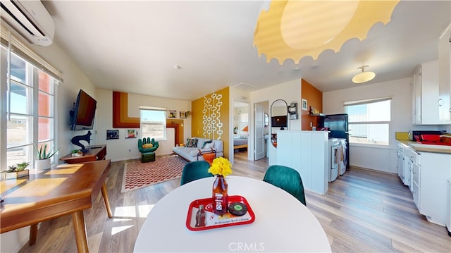 dining area featuring light hardwood / wood-style flooring, a healthy amount of sunlight, an AC wall unit, and washing machine and dryer