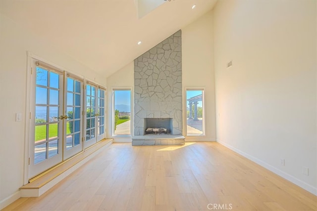 unfurnished living room with light hardwood / wood-style floors, a stone fireplace, and high vaulted ceiling