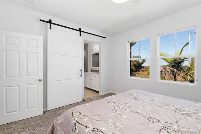 bedroom featuring a barn door, light colored carpet, and ensuite bath